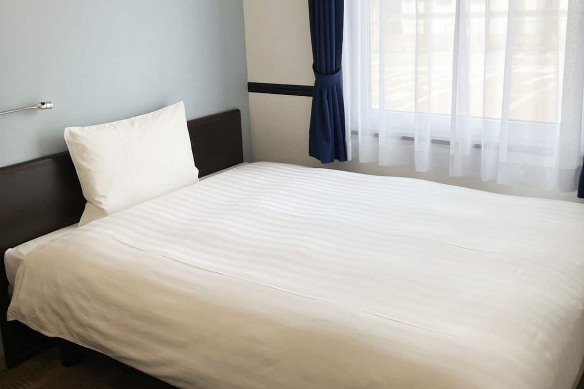 Un lit bien fait, avec du linge de lit blanc, dans une chambre d’hôtel.