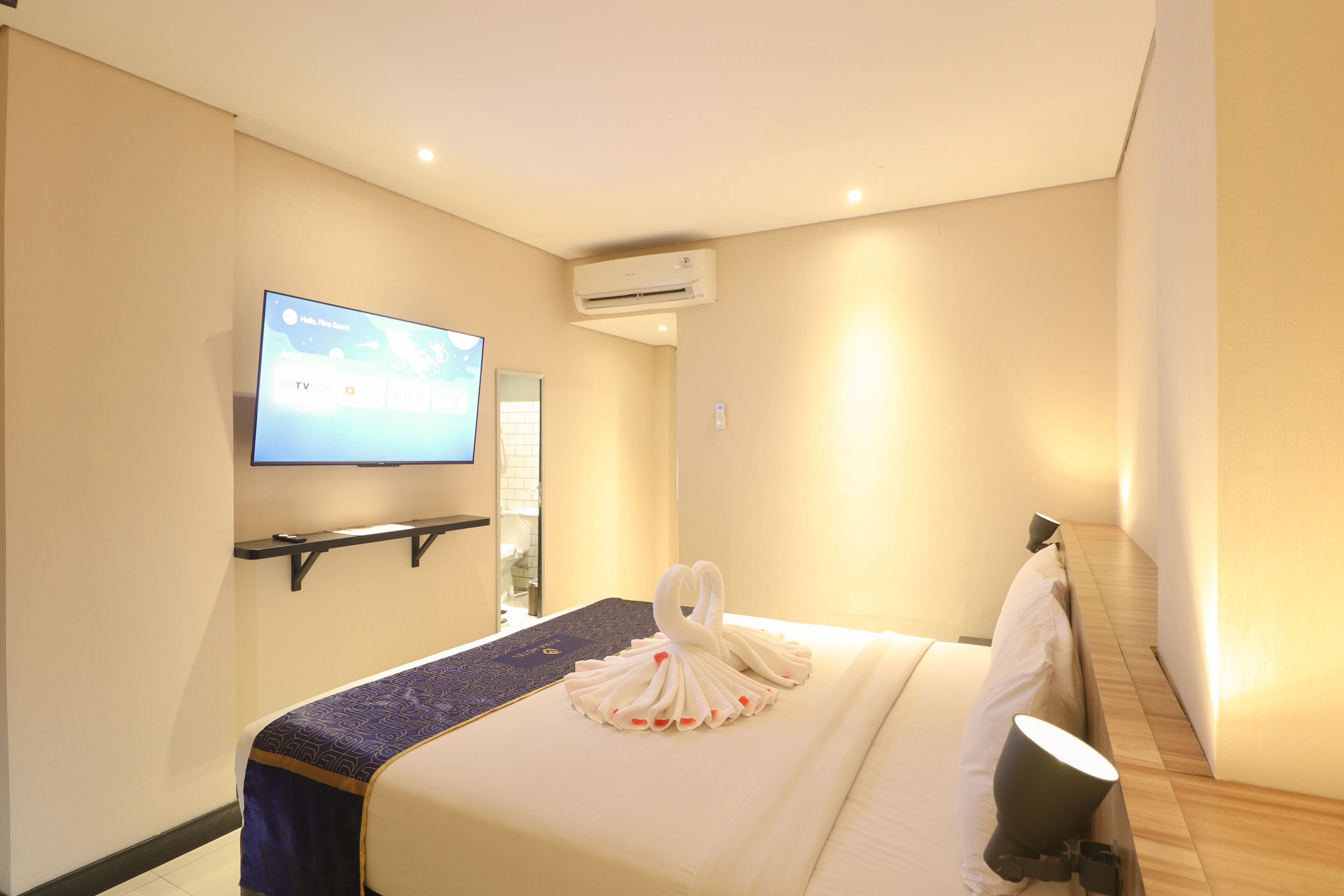A hotel room with a bed, a TV mounted on the wall, and an air conditioning unit.