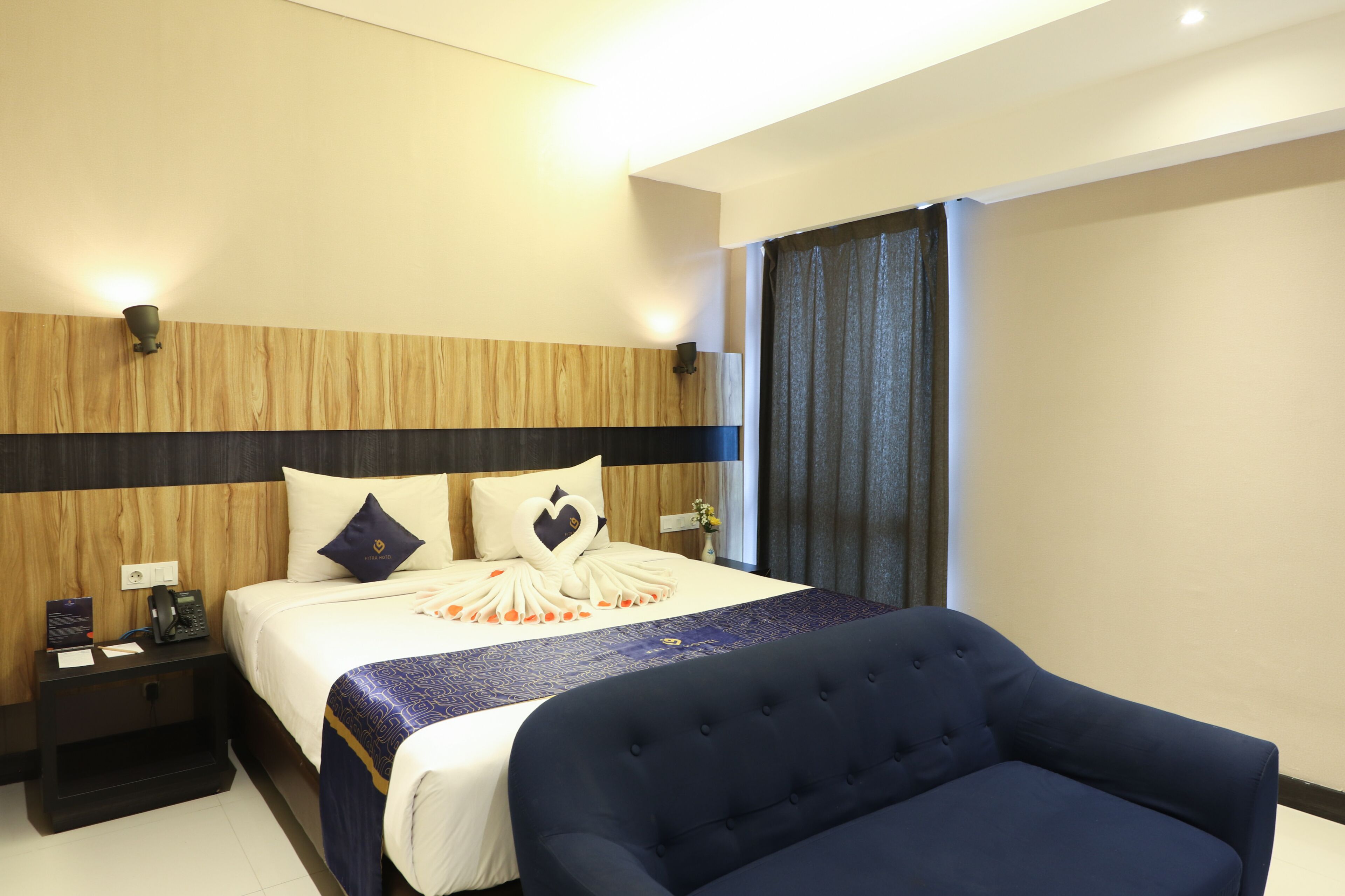 Ein Hotelzimmer mit einem Bett, einem Nachttisch, einem blauen Sessel und einem Fenster mit Vorhängen.