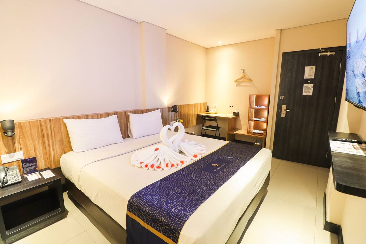 Una habitación de hotel con una cama bien hecha, un escritorio, una silla y un televisor.