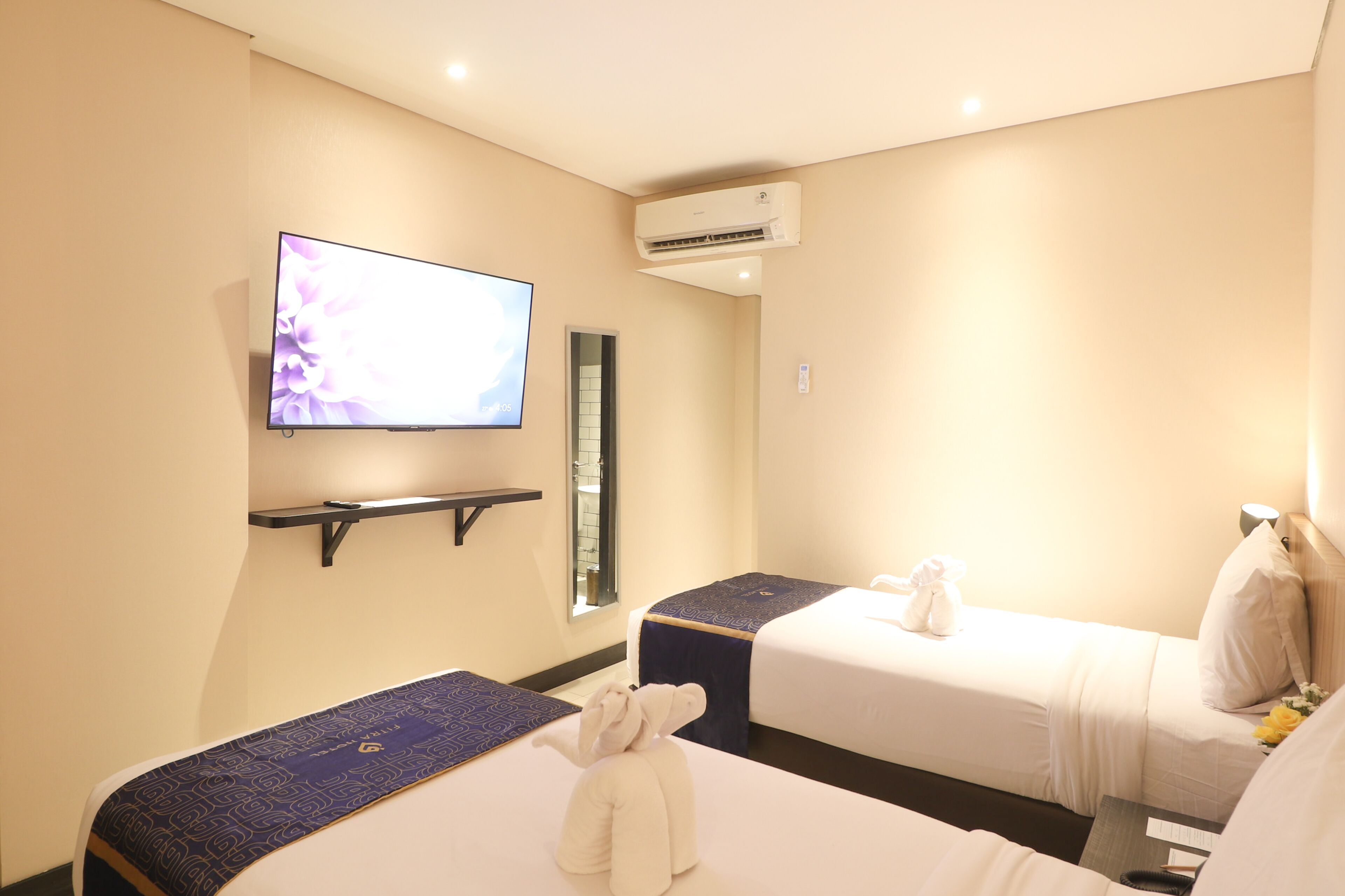 A hotel room with two beds, a TV, an air conditioner, and a small shelf.