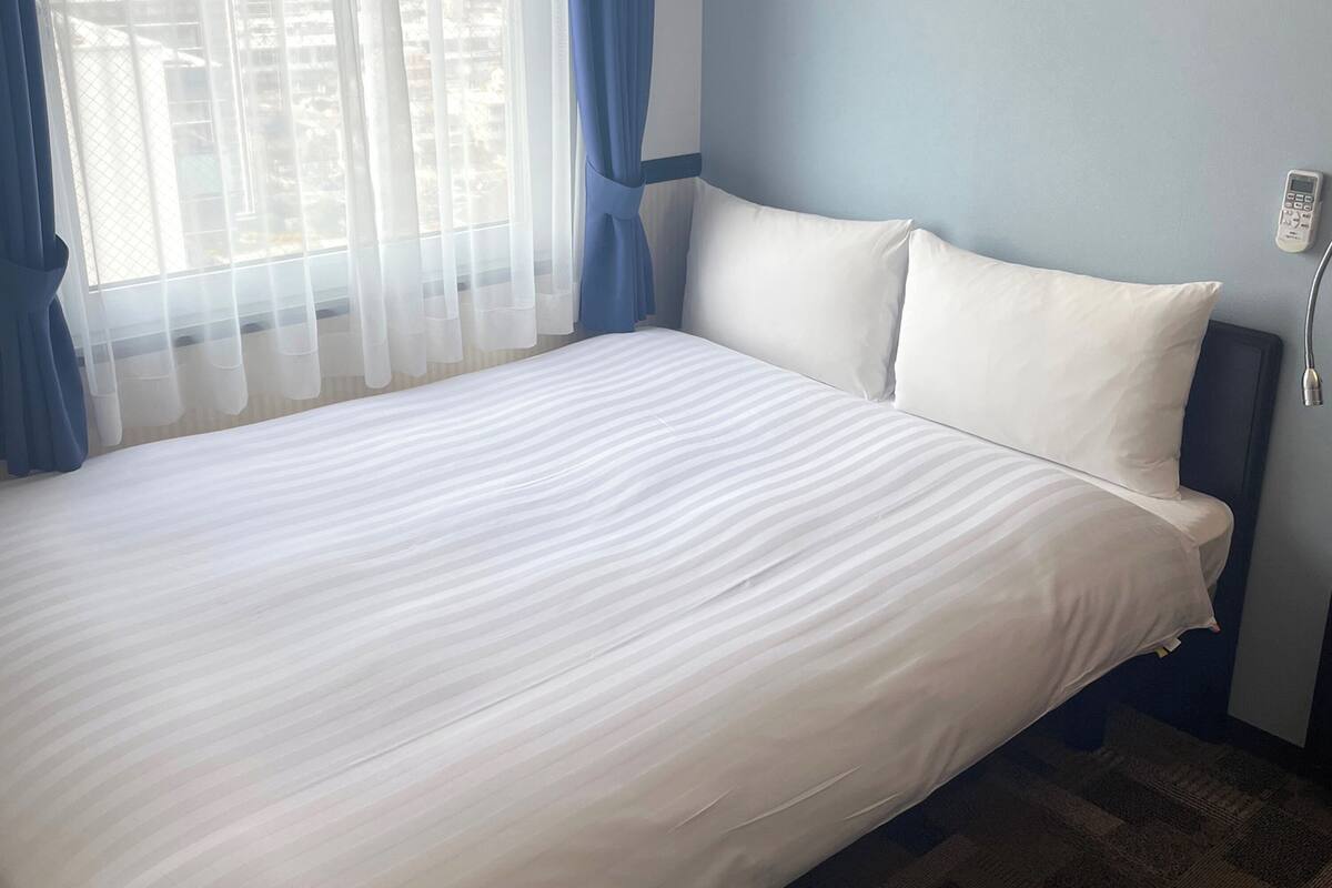 A hotel room with a large bed, white bedding, a blue wall, and a window with sheer curtains.