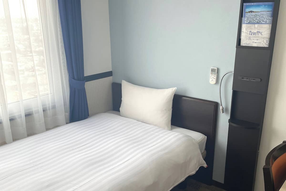 A hotel room with a bed, a nightstand, a desk, and a window with curtains.