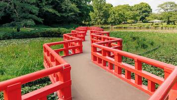 A red bridge in a park with lush greenery and trees in the background.