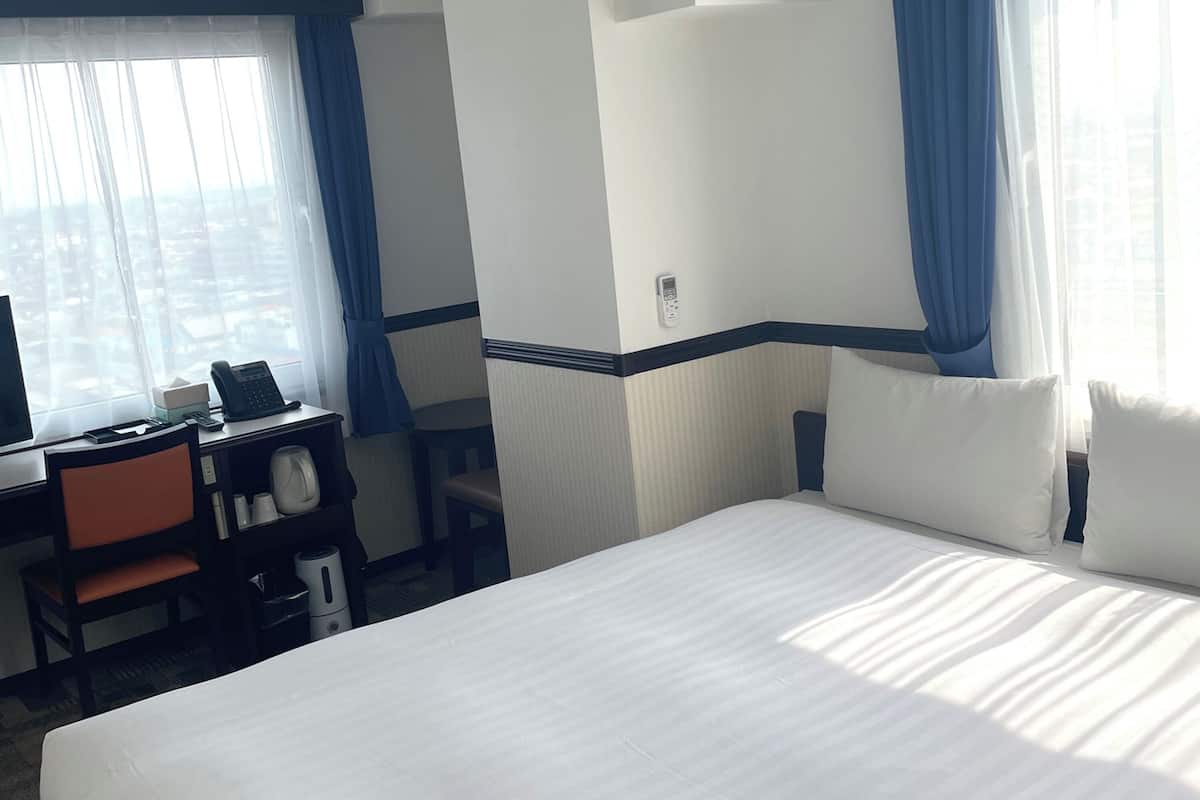 A hotel room with a large bed, a desk with a telephone, and a chair.