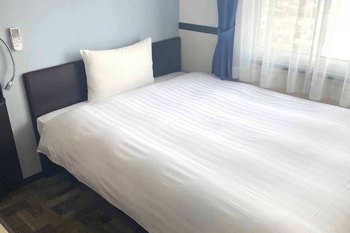 A neatly made bed with white linens in a hotel room.