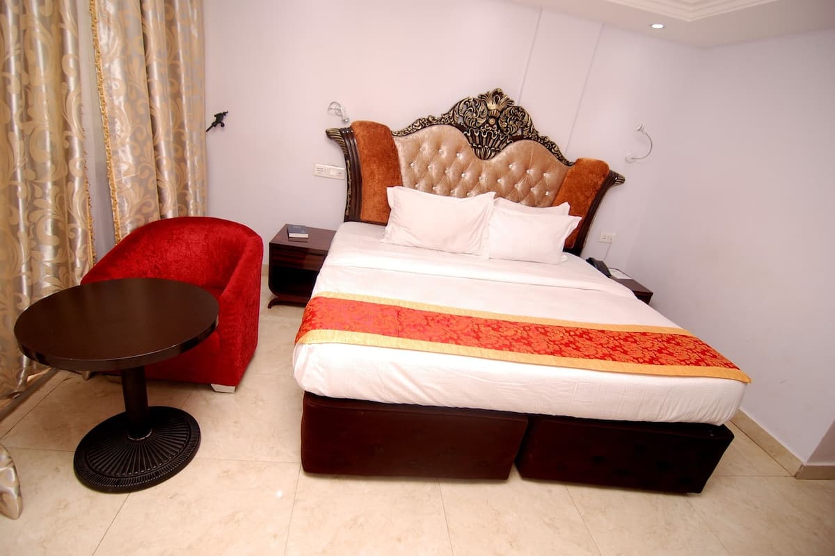Habitación de hotel con una cama grande, un sillón rojo, una mesita redonda y un cabecero decorativo.