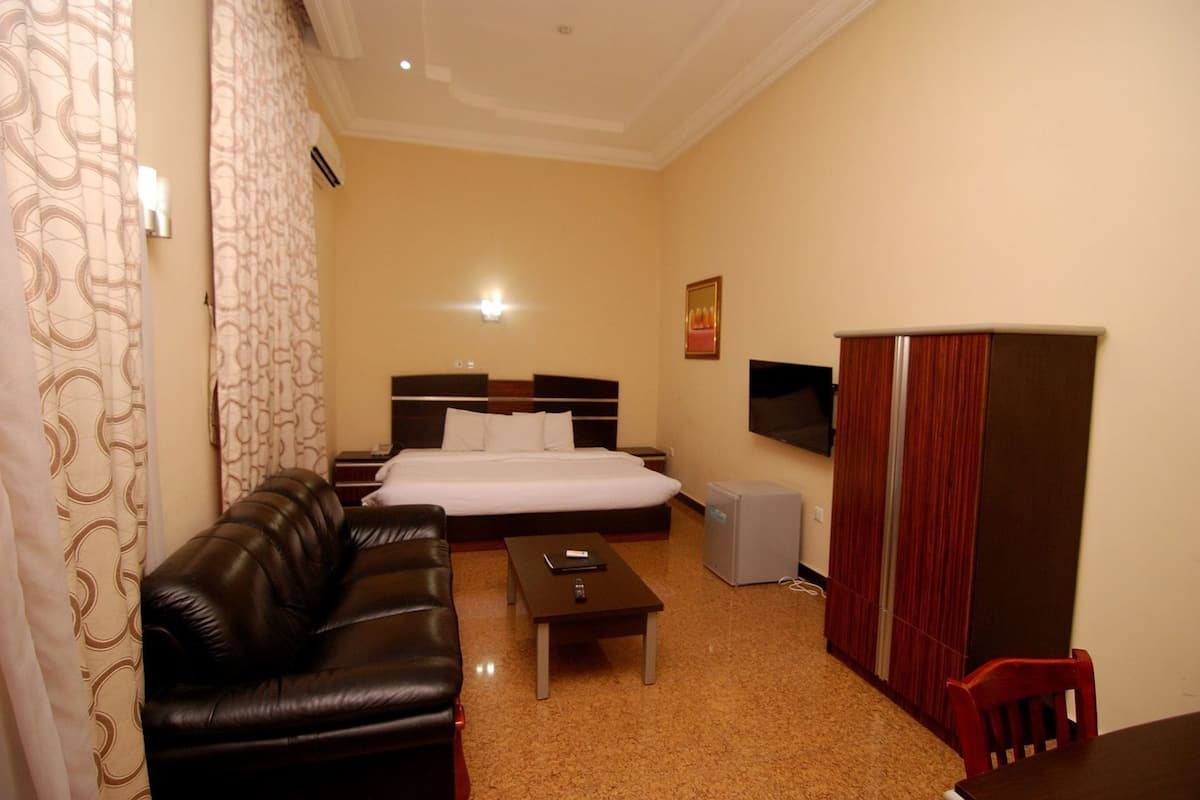 Una habitación de hotel con cama, sofá de cuero, mesita, televisor y armario.
