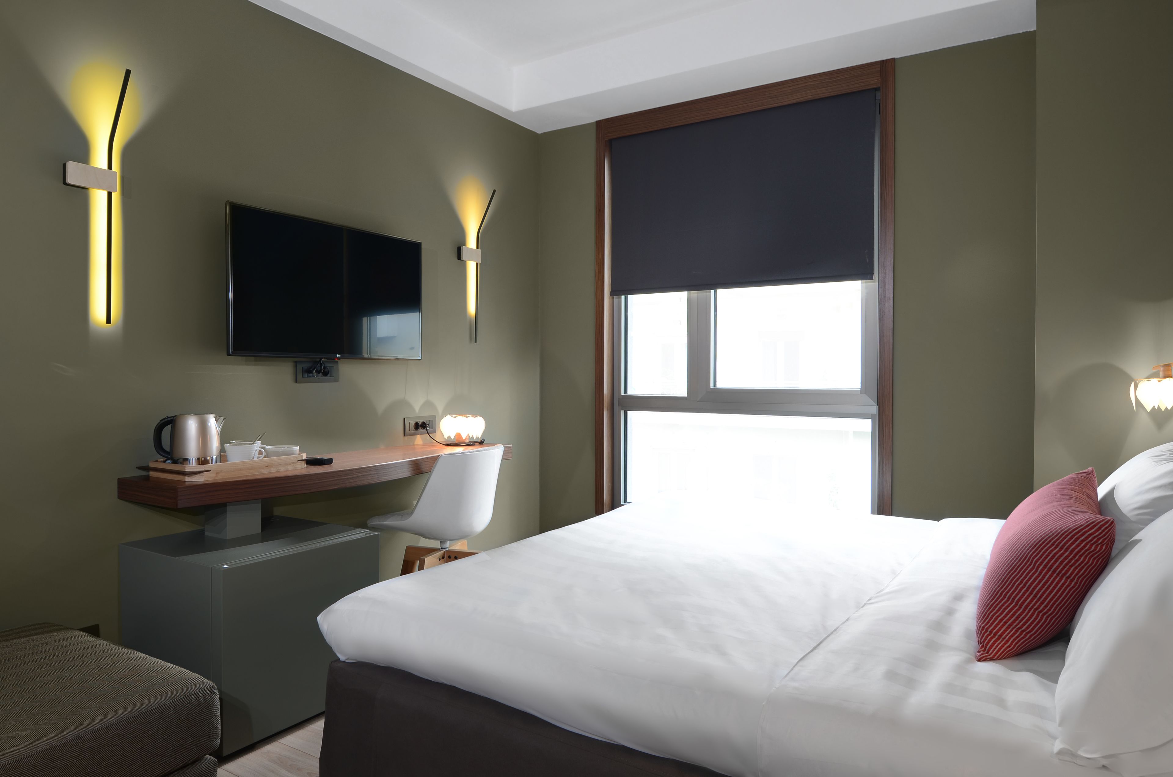 Ein Hotelzimmer mit einem Bett, einem Schreibtisch mit Stuhl, einem Fernseher und Wandleuchten.