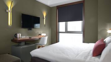 Ein Hotelzimmer mit einem Bett, einem Schreibtisch mit Stuhl, einem Fernseher und Wandleuchten.