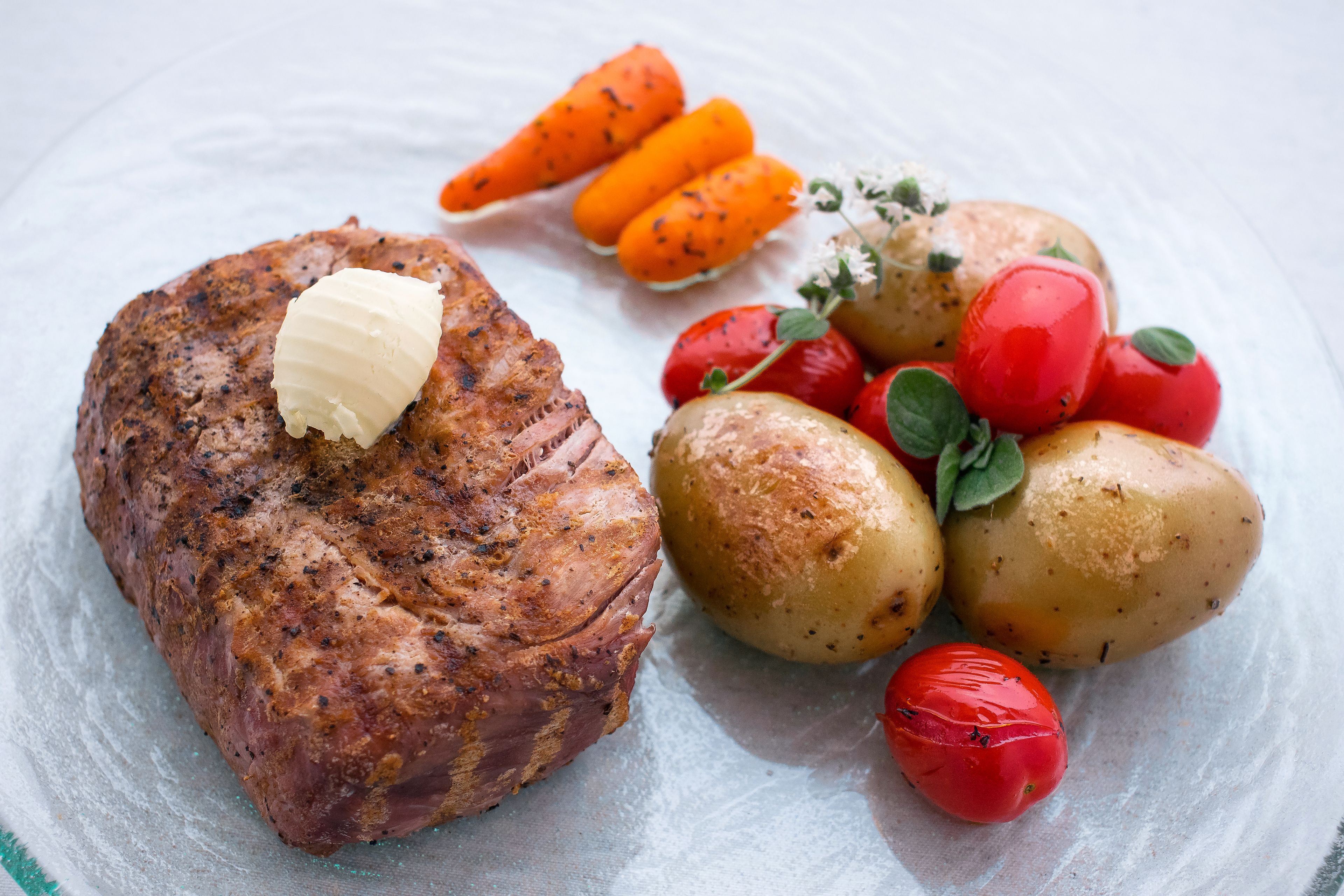 Ein Teller mit Fleisch, belegt mit Butter, dazu Bratkartoffeln und Kirschtomaten.