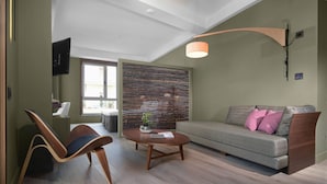 A modern living room with a sofa, a wooden chair, a coffee table, and a TV mounted on the wall. - Lake Spirit Boutique Hotel & Spa (Ioannina)