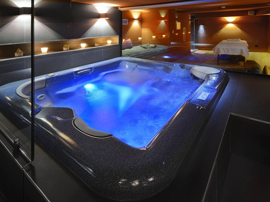 A modern spa room with a heated blue pool, a massage table, and ambient lighting.
