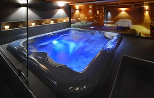 Un moderno spa con piscina azul climatizada, camilla de masaje e iluminación ambiental.