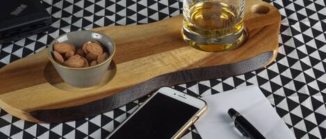 Un teléfono inteligente, una copa de whisky, un cuenco de almendras, un bolígrafo y un ordenador portátil sobre un mantel a cuadros.
