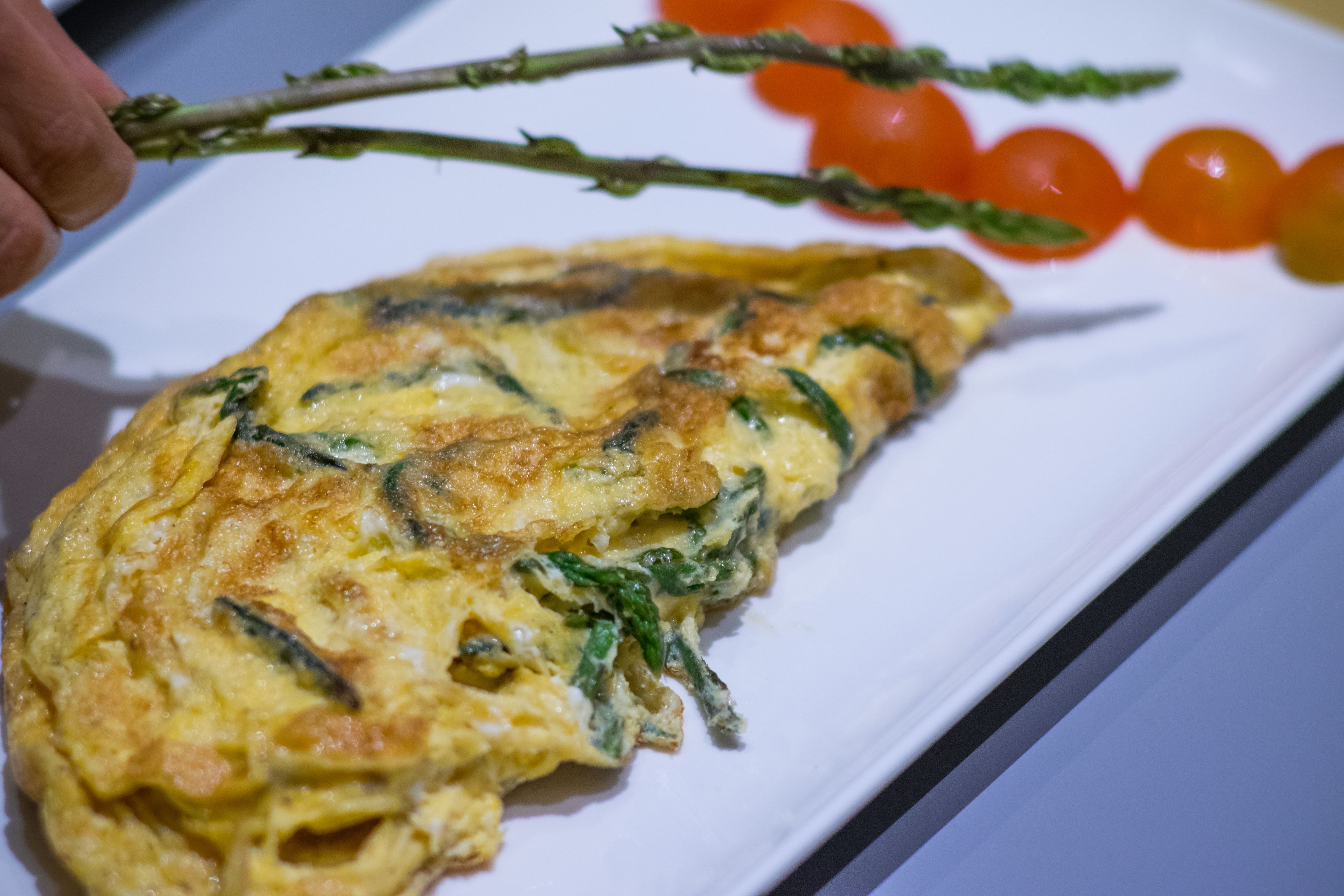 A plate with an omelette, cherry tomatoes, and asparagus.