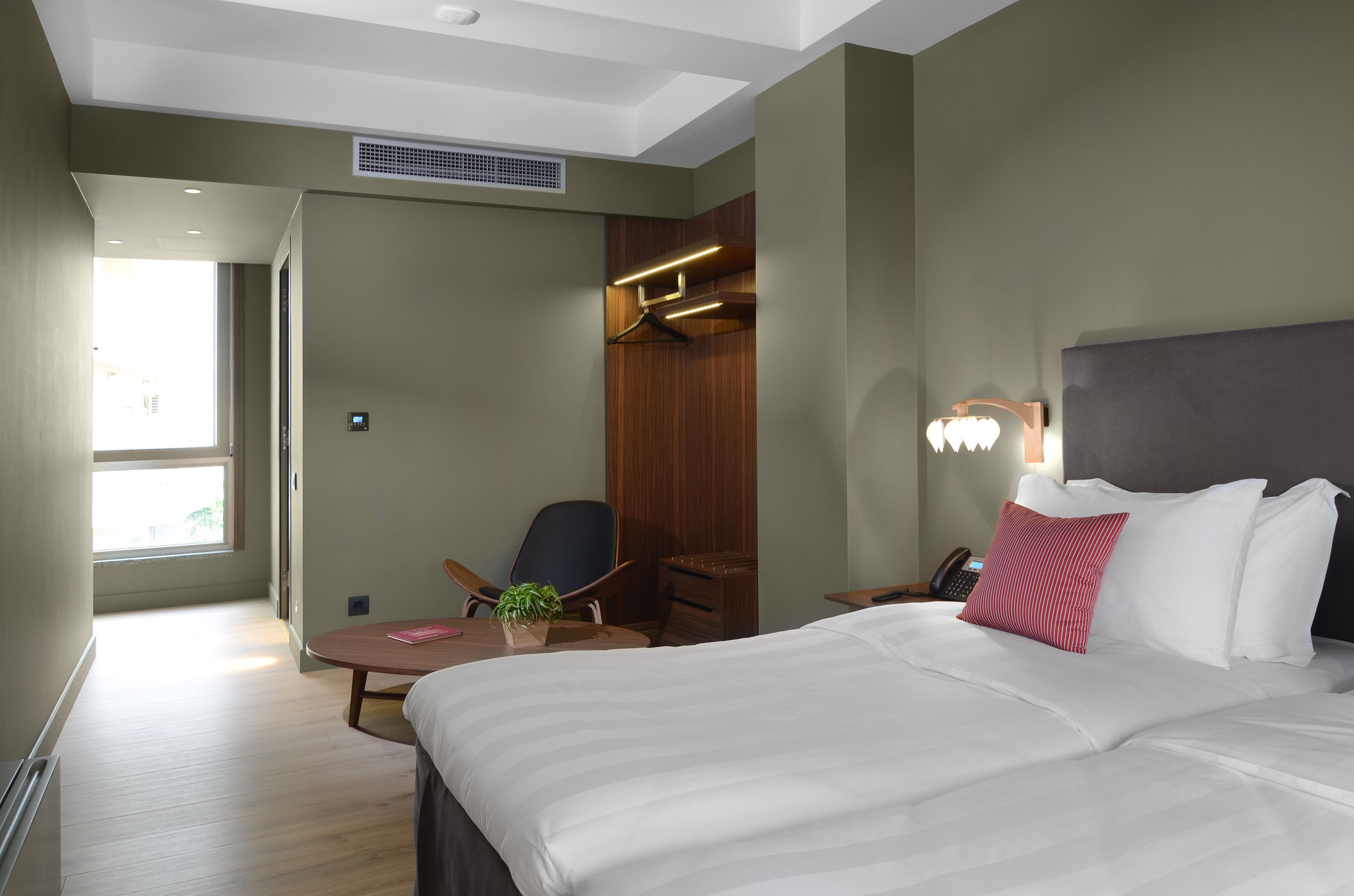 A hotel room with a bed, a desk, a chair, a hanging coat rack, and a window.