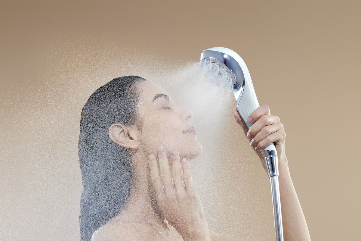 Une personne utilise un pommeau de douche portatif, et l’eau jaillit tout autour d’elle.
