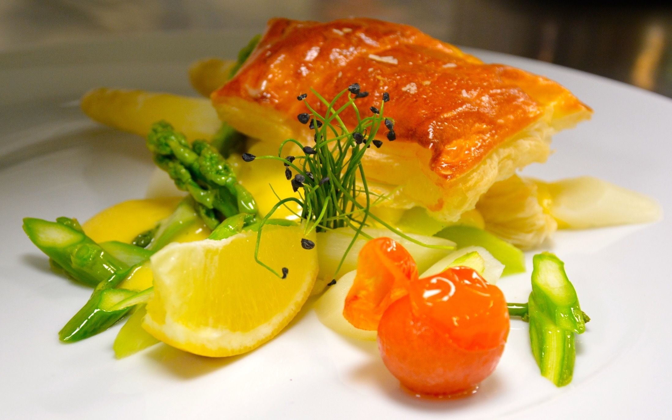 Een bord met zalm, asperges, citroen en kerstomaatjes.
