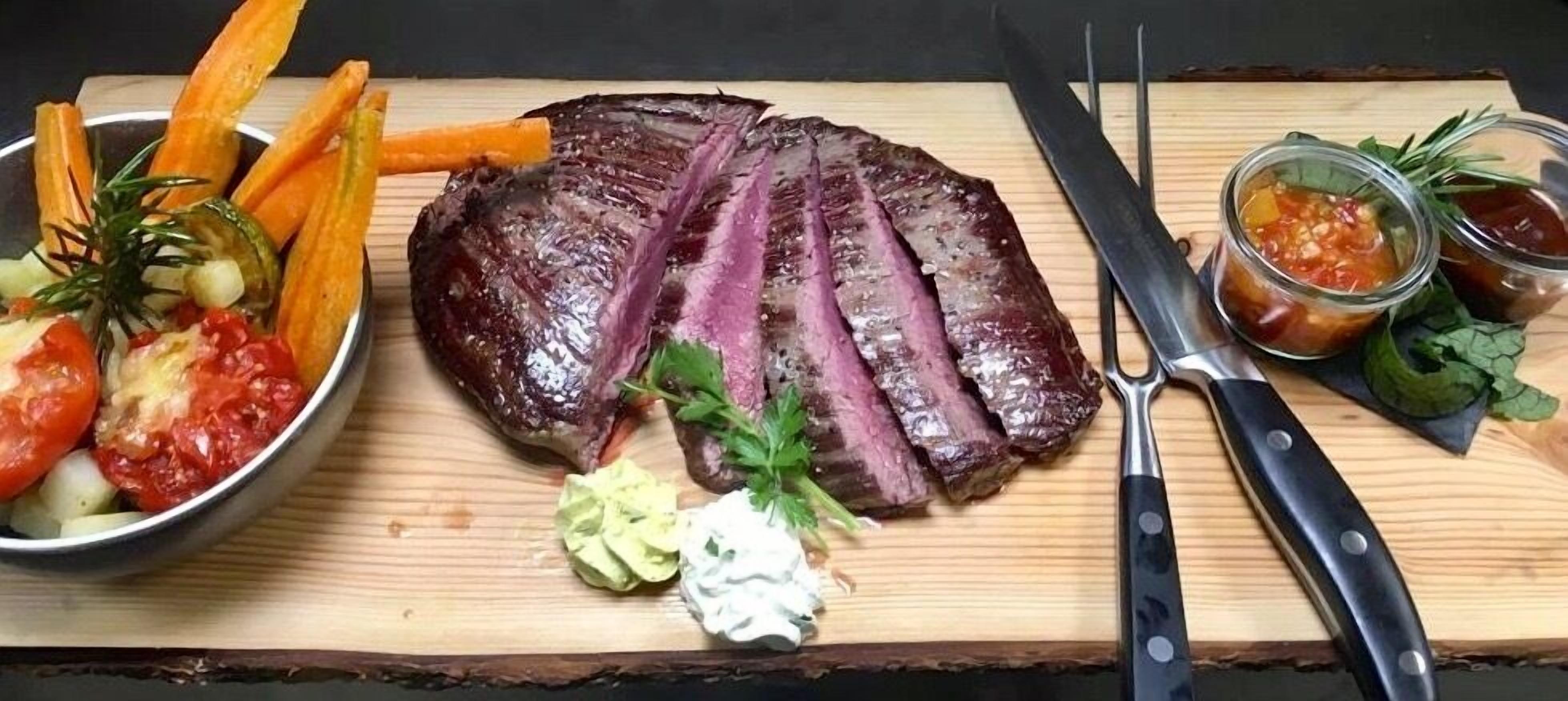 Ein Steak mit geschnittenem Fleisch, Garnituren und Beilagen auf einem Holzbrett.