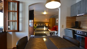 A compact kitchen with a dining area, a bed in the background, and a visible oven. - Gasthof Hotel Hirschen (Kleines Wiesental)
