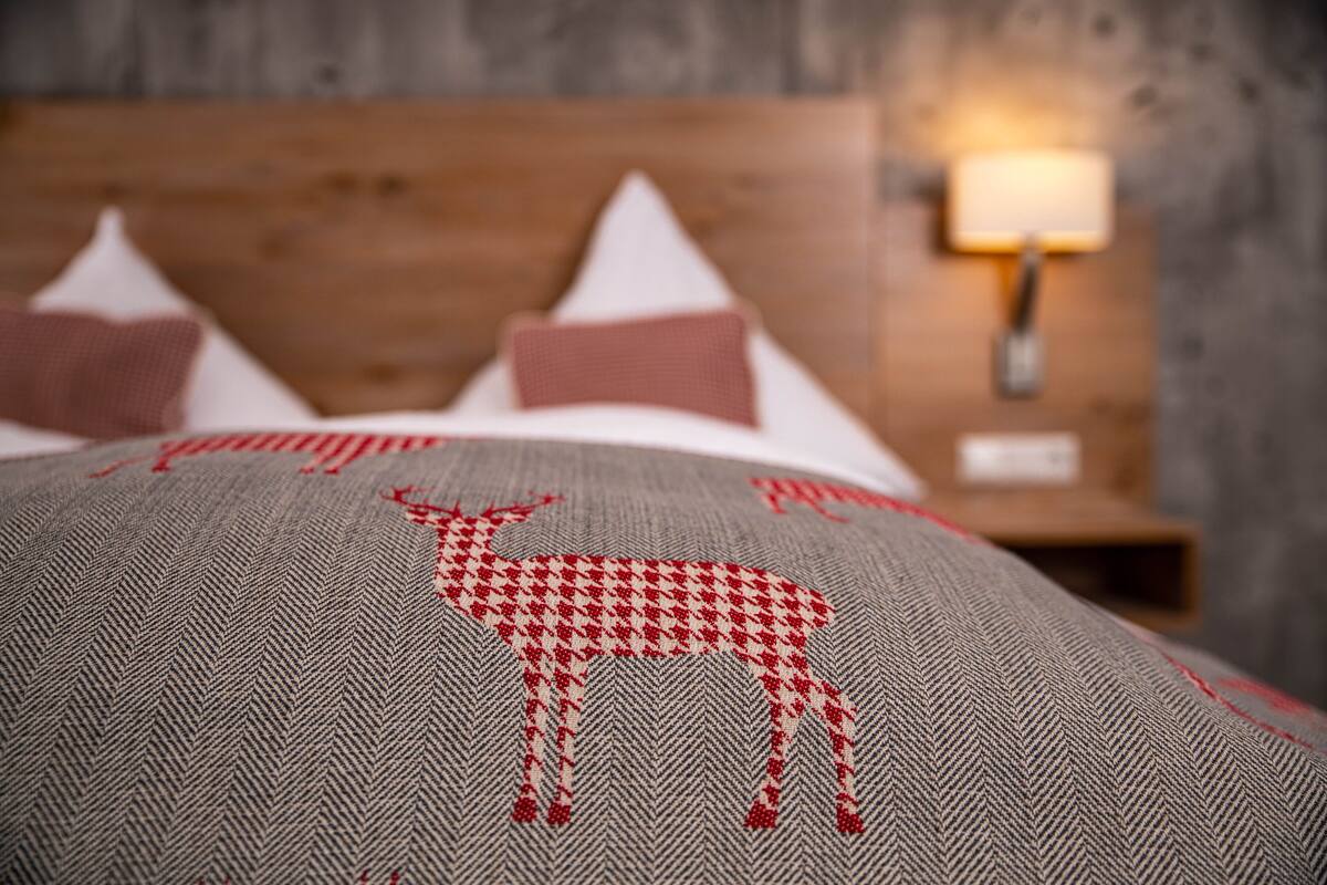 A bed with a patterned pillow featuring a red and white design, a wooden headboard, and a nightstand with a lamp.