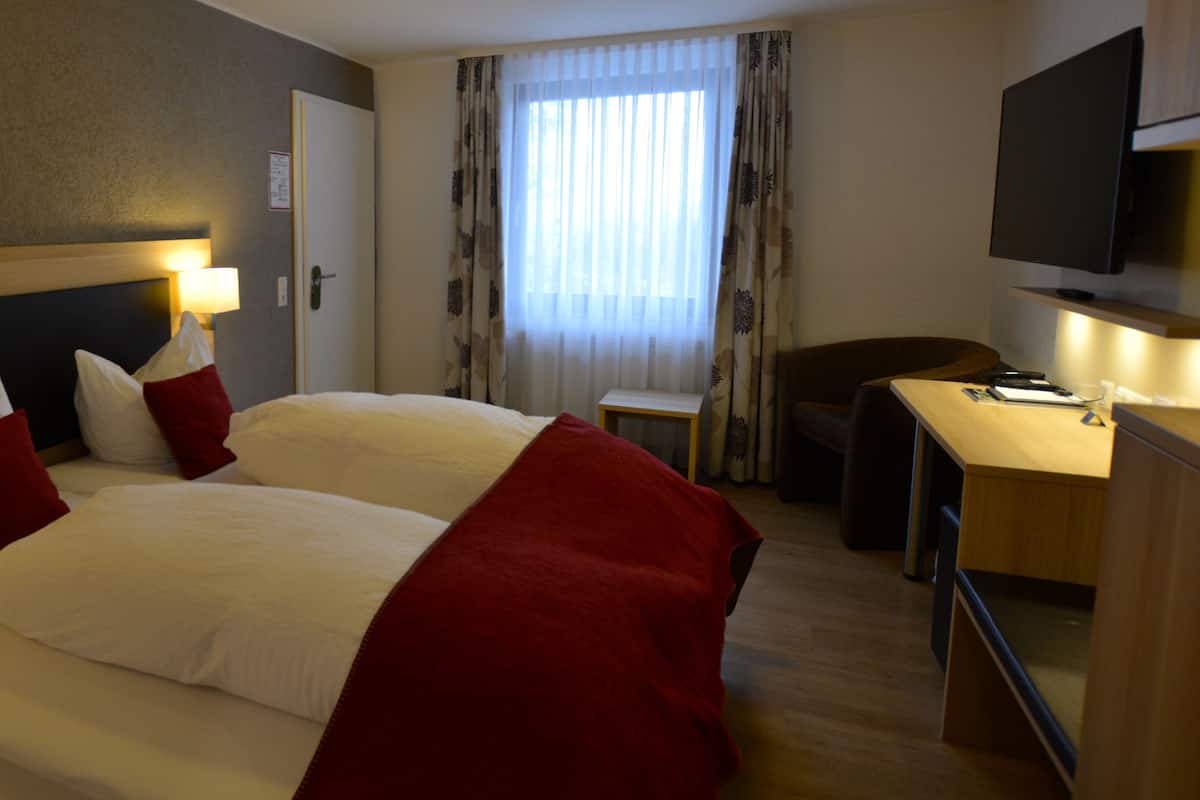A hotel room with a large bed, bedside tables, a desk, and a TV.