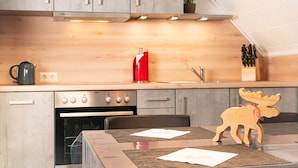 A modern kitchen with wooden cabinets, a built-in oven, and a red kettle. - Gasthof Hotel Hirschen (Kleines Wiesental)