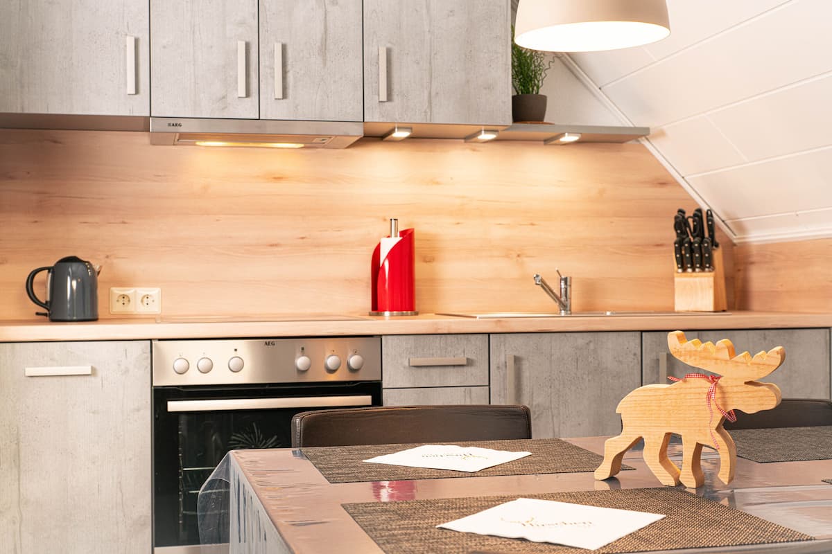 A modern kitchen with wooden cabinets, a built-in oven, and a red kettle.