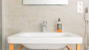 Un lavabo blanc dans une salle de bain, avec un robinet chromé, un flacon de savon et un miroir au-dessus.