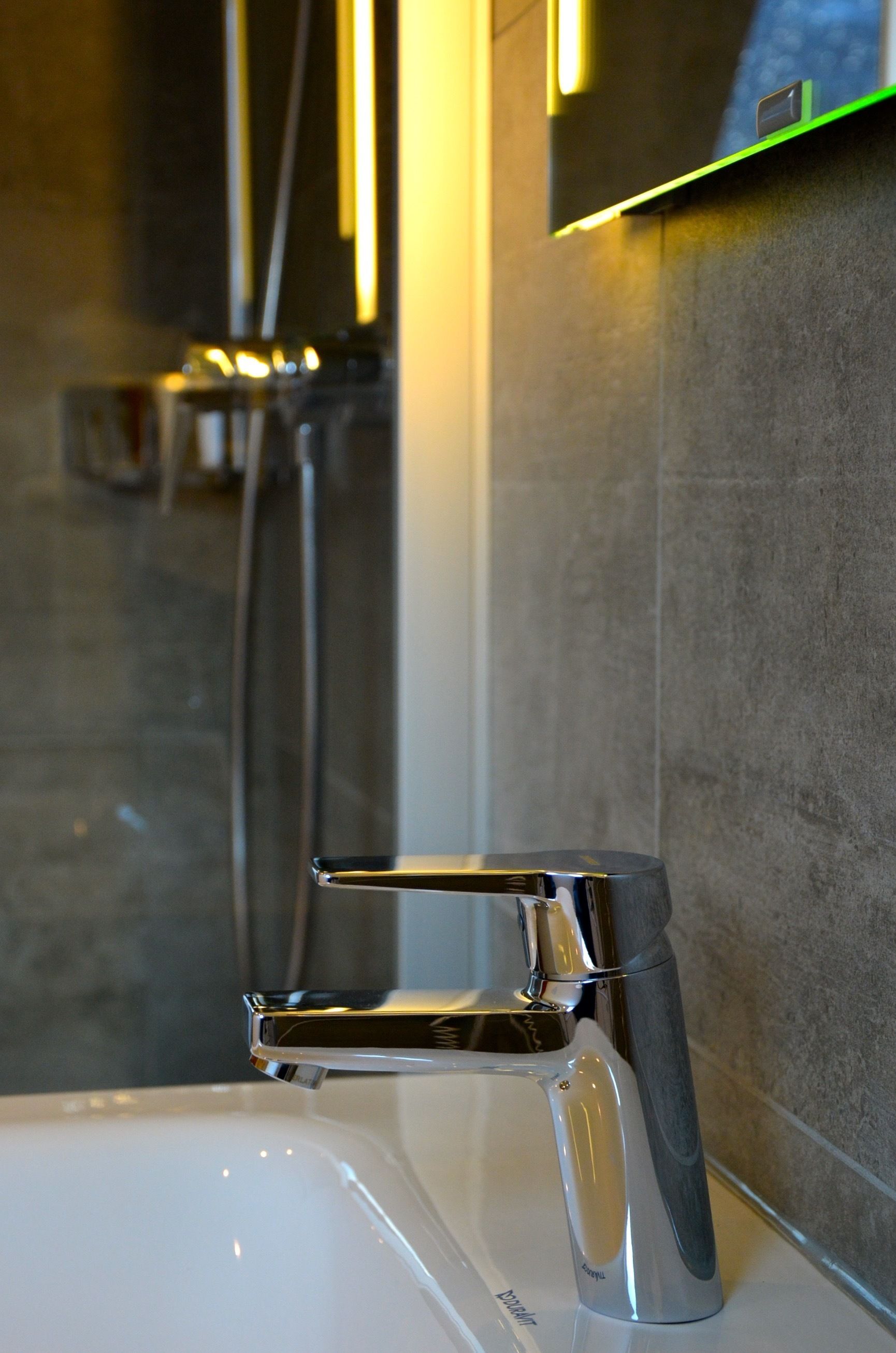Ein modernes Badezimmer mit einem chromfarbenen Wasserhahn, einer Handbrause und einer wandmontierten Bedienkonsole.