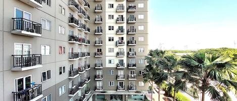 A multi-story residential building with balconies, a swimming pool, and palm trees.