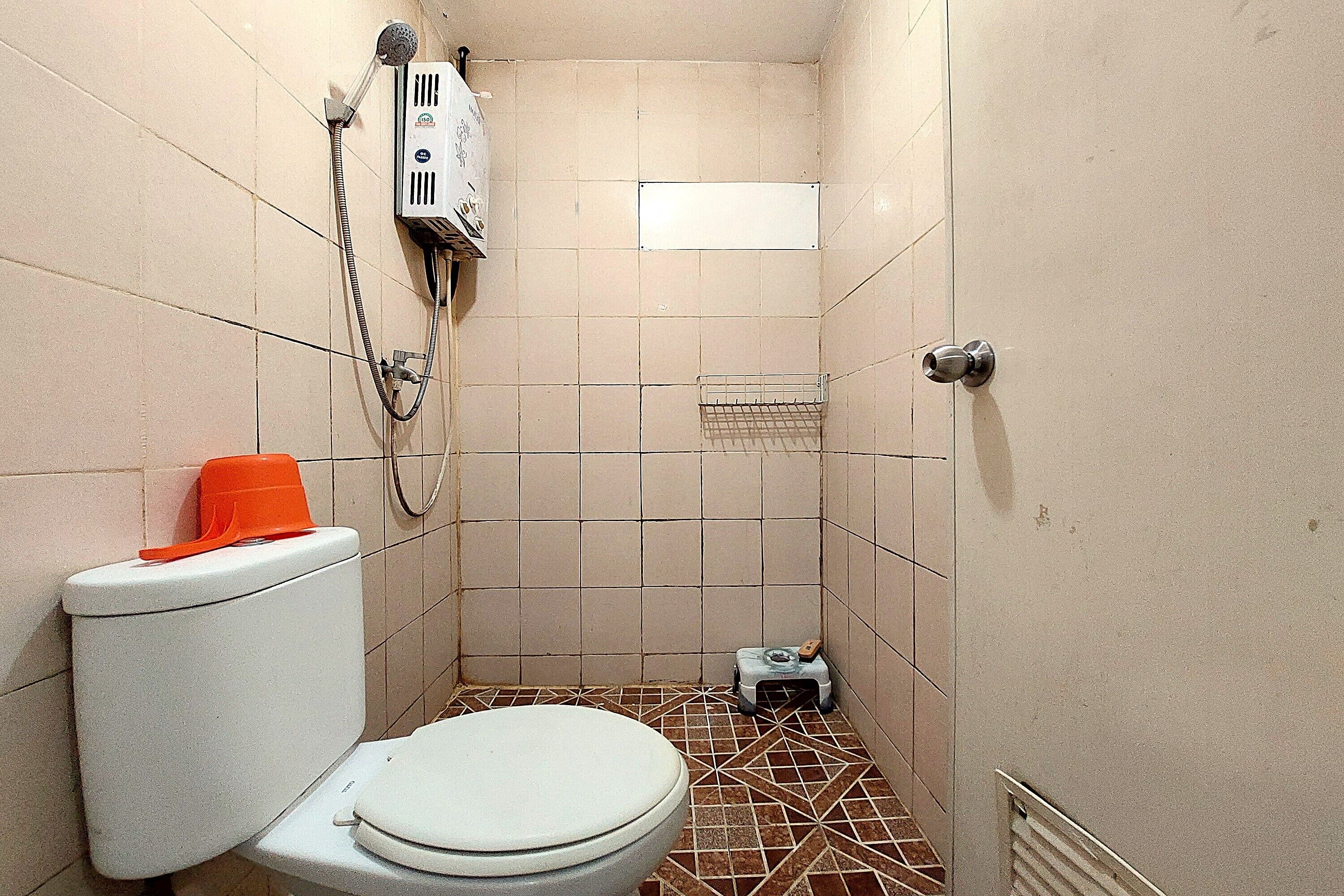 A small, tiled bathroom with a toilet, a shower unit, and a small shelf.