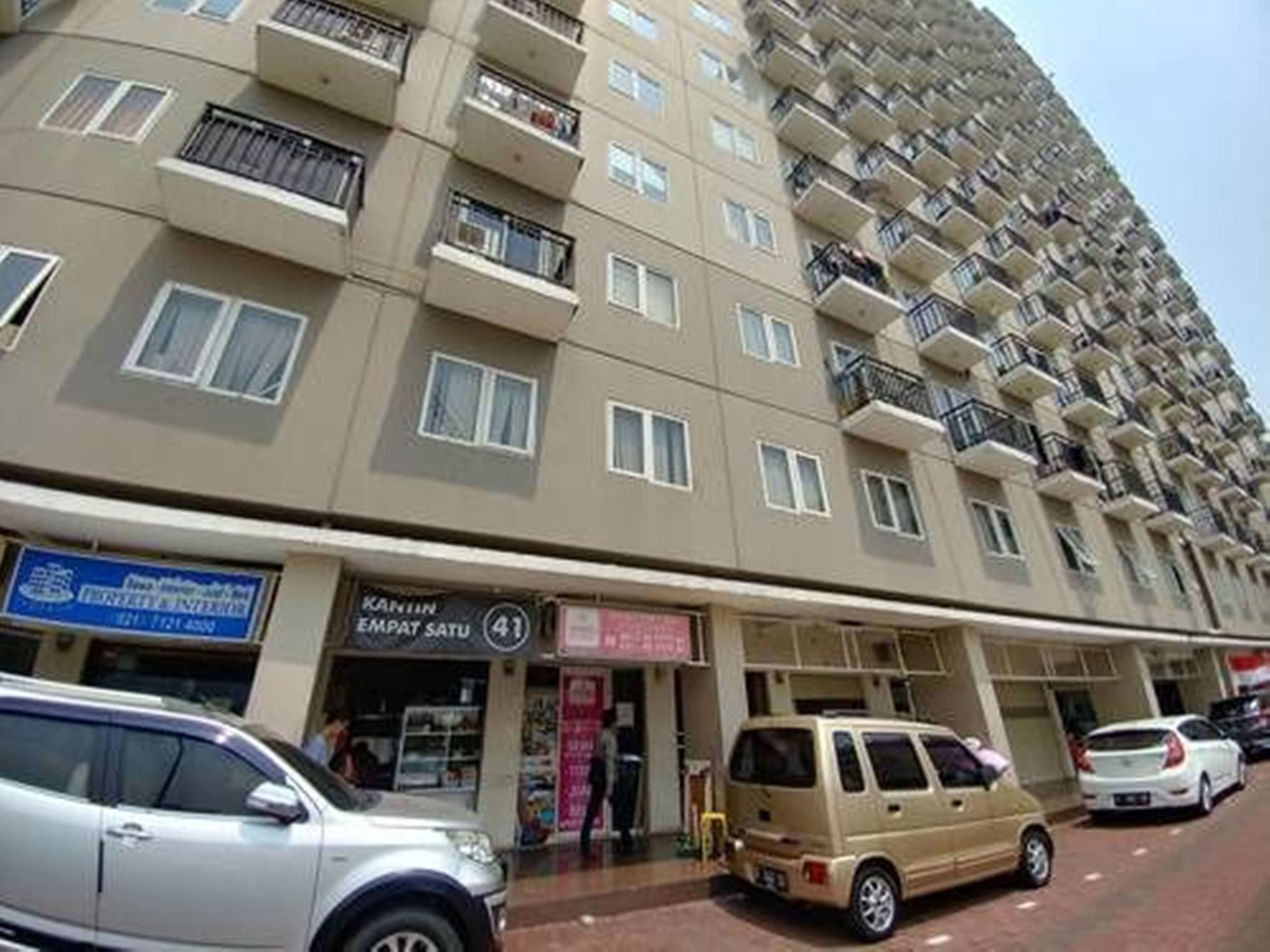 A multi-story residential building with balconies, a visible shop on the ground floor, and parked cars.