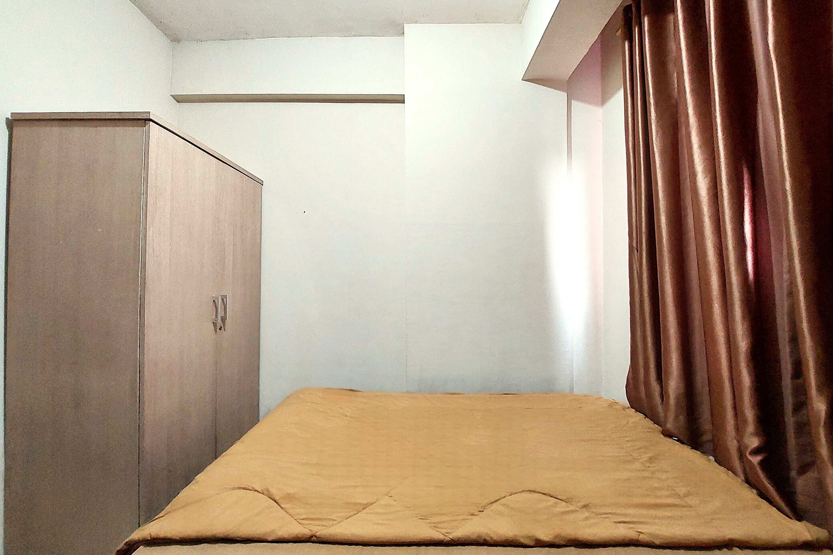 A small, single-bed room with a wooden wardrobe and a brown curtain.