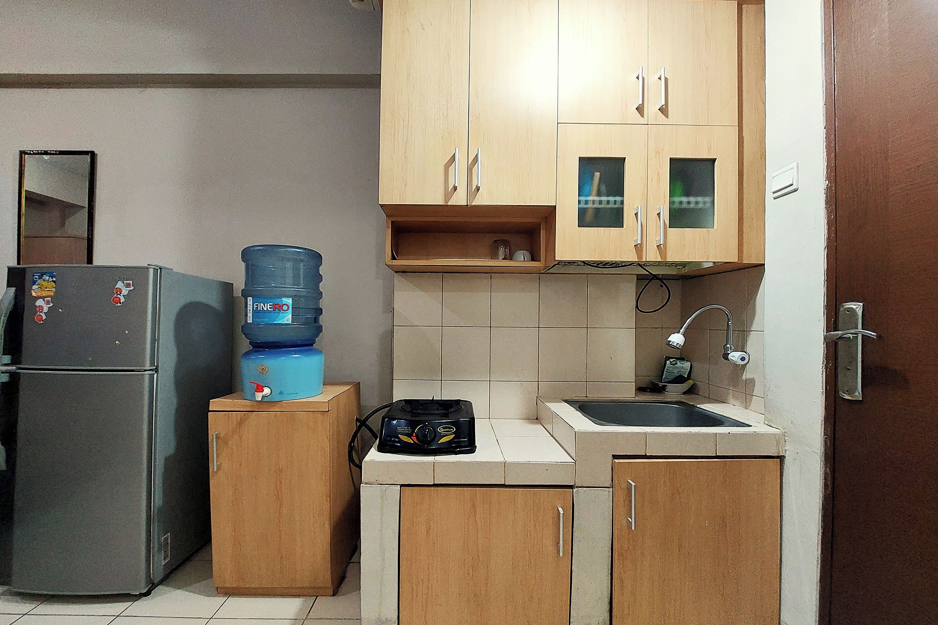 A compact kitchen with a refrigerator, a water dispenser, a gas stove, and wooden cabinets.