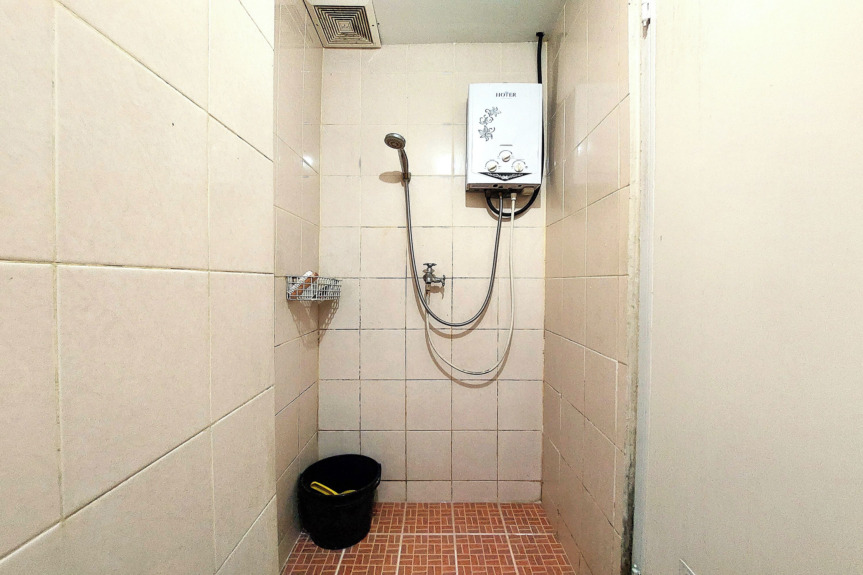 A small, tiled shower room with a built-in heater, a showerhead, and a bucket.