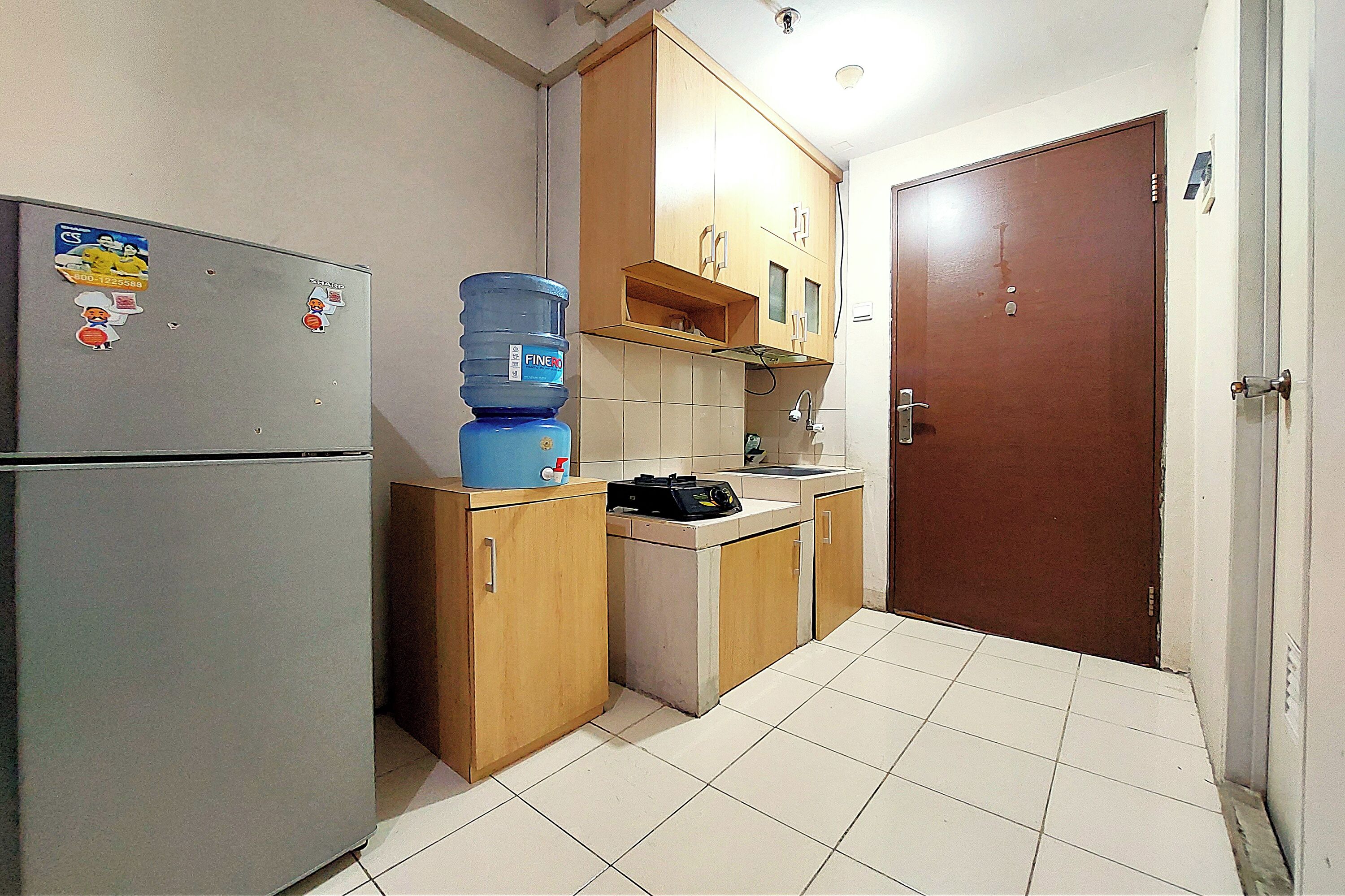 A compact kitchen with a refrigerator, a water dispenser, and wooden cabinets.