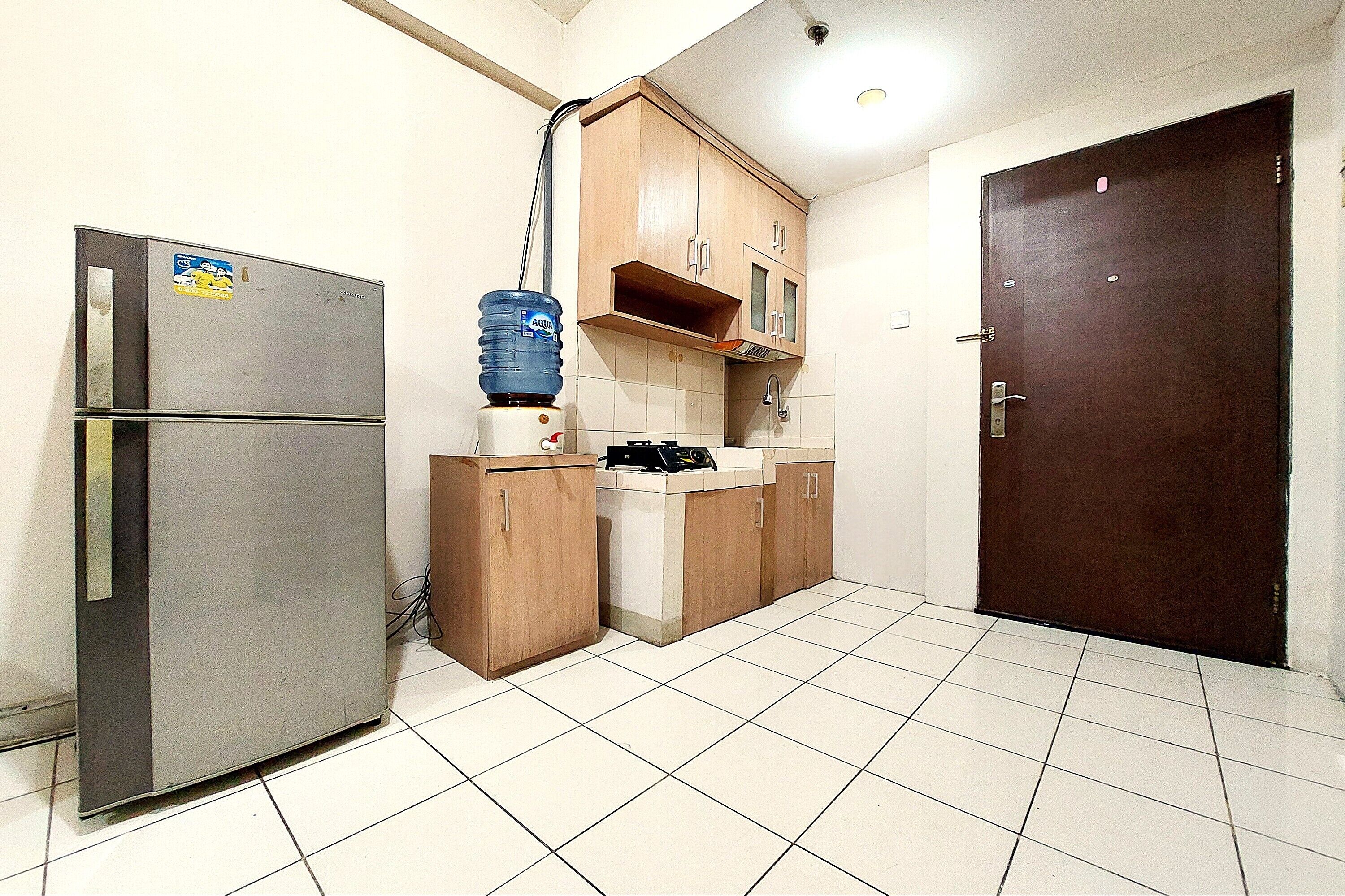 A compact kitchen with a refrigerator, wooden cabinets, a water dispenser, and a tiled floor.