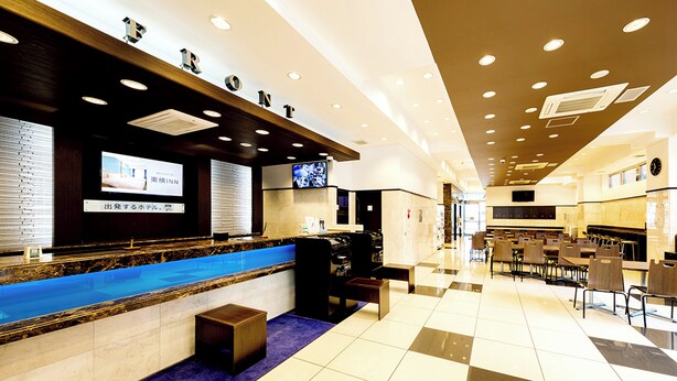 A hotel reception area with a check-in counter, a television screen, and a seating area with tables and chairs. - Toyoko Inn Kintetsu Yokkaichi-eki Kita-guchi (Yokkaichi)