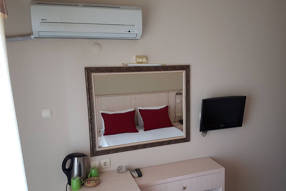 A hotel room with a bed, a bedside table, a mirror, a TV, and an air conditioner.