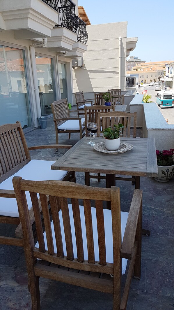 An outdoor seating area with wooden tables and chairs, a potted plant, and a view of the street.