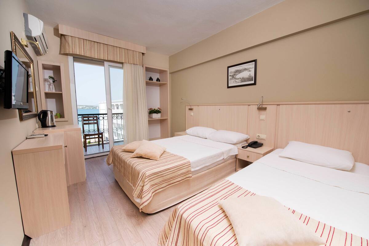 A hotel room with two beds, a desk, a chair, a TV, and a balcony with a view.