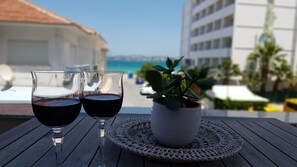 Two wine glasses on a table with a woven placemat, a potted plant, and a view of a building and the sea in the background.