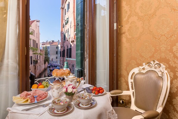 A table set with food and drink items, a chair, and a view of a city street through a window. - Residenza Veneziana (Venice)