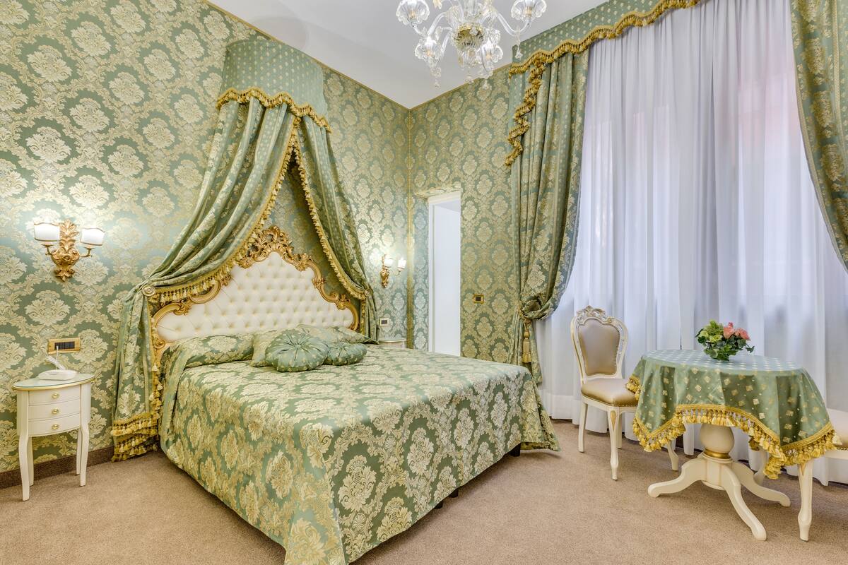 A bedroom with a large bed, a vanity, a chair, and a table with a floral tablecloth.