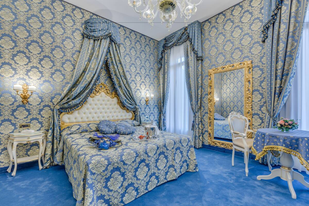 A bedroom with a large bed, ornate curtains, a chandelier, and a mirror with a gold frame.