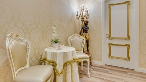 A room with two ornate chairs, a table with a white tablecloth, and a statue of a person holding a candelabra. - Residenza Veneziana (Venice)