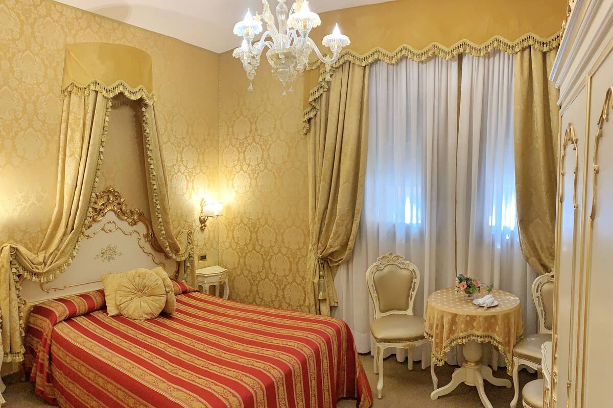 A luxurious bedroom with a large bed, ornate curtains, a chandelier, and a small round table with chairs.