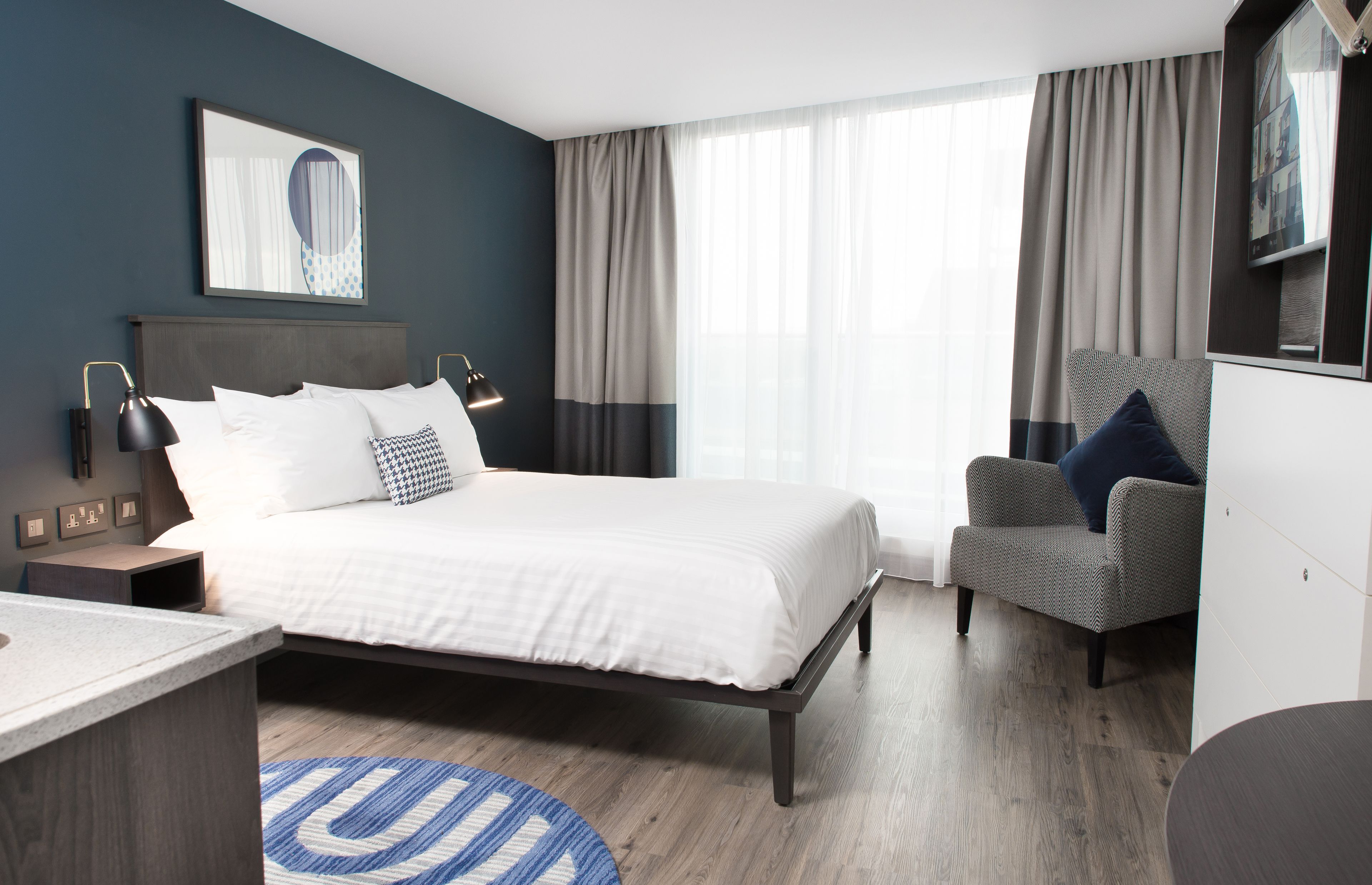 Quarto de hotel moderno com uma cama grande, área de estar e uma mesa de trabalho.